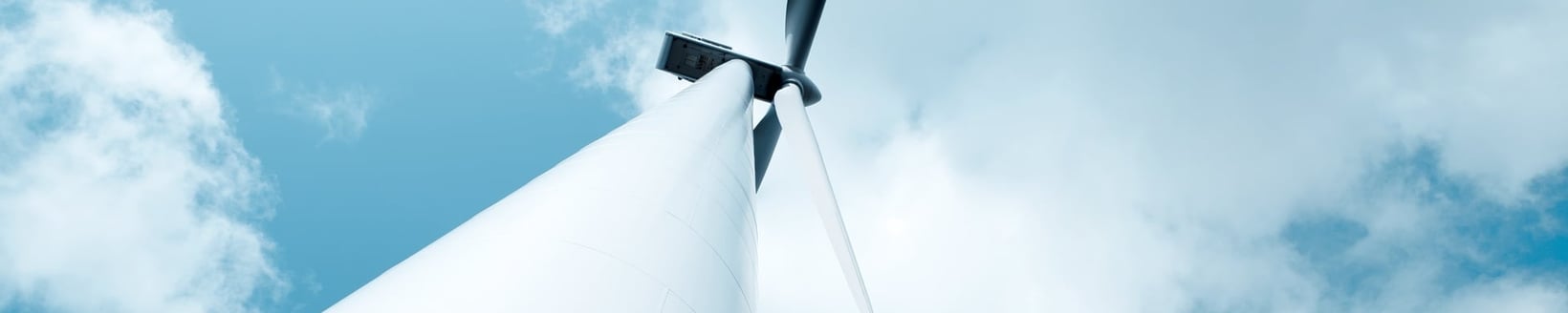 Ett vindkraftverk reser sig över betraktaren, där rotorbladen syns mot en molnig himmel.