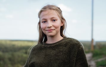 En flicka klädd i en grön tröja tittar in i kameran.