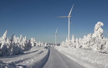 En väg och två vindkraftverk i snötäckt landskap En väg och två vindkraftverk i snötäckt landskap